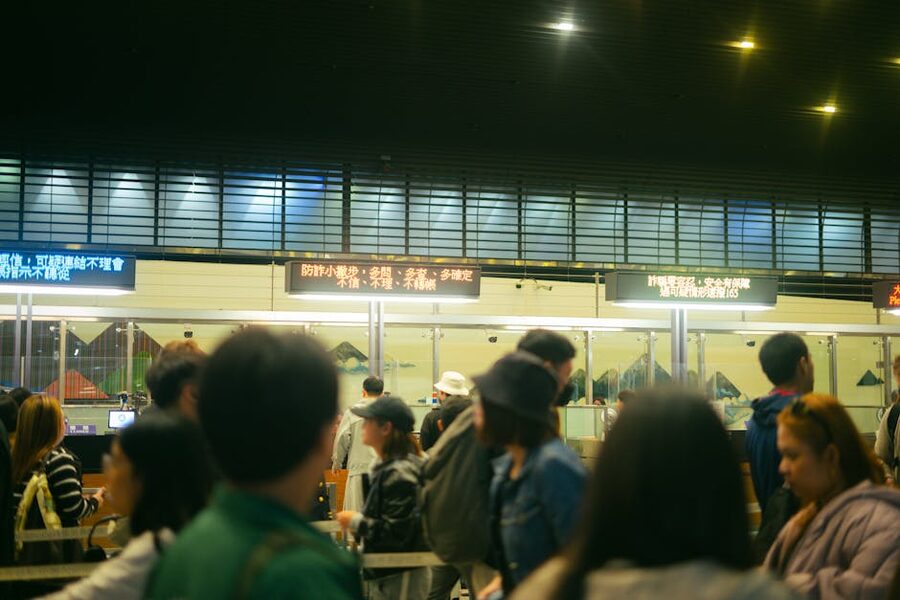 Busy airport check-in counter with queue of passengers and flight information signs overhead