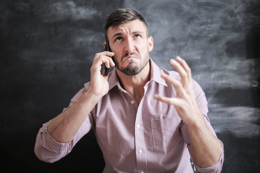 Adult man in pink dress shirt looking stressed while on phone call
