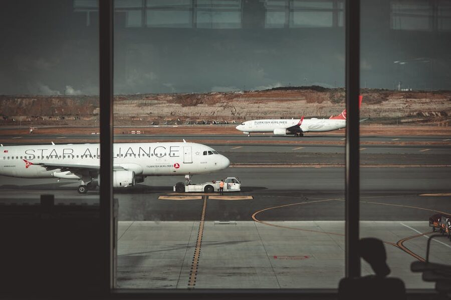 Commercial airliners lined up on tarmac seen through airport windows